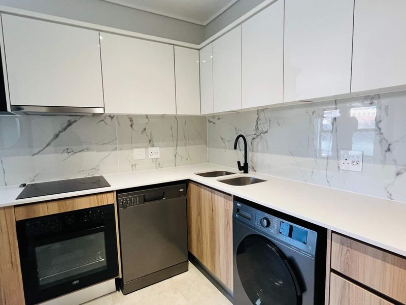 Modern kitchen featuring sleek white cabinetry, marble-look splashback, stone countertops, integrated oven, hob, extractor fan, and a double sink with a contemporary mixer tap.