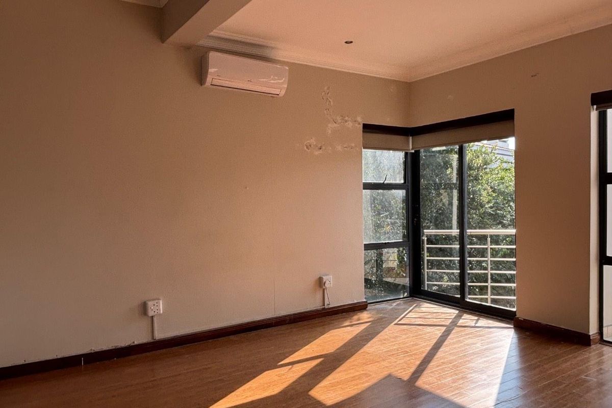 An empty bedroom featuring laminate flooring, a wall-mounted air conditioning unit, and large sliding glass doors leading to a balcony.