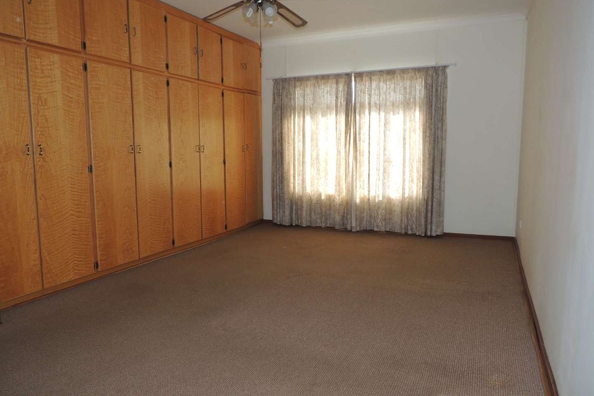 Spacious bedroom featuring extensive built-in wooden cabinetry, carpeted flooring, and a ceiling fan, offering a blank canvas for personalization.