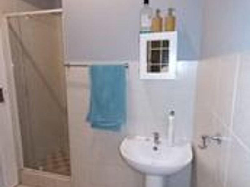 A functional bathroom featuring a pedestal basin, tiled walls and flooring, and a glass-enclosed shower unit.