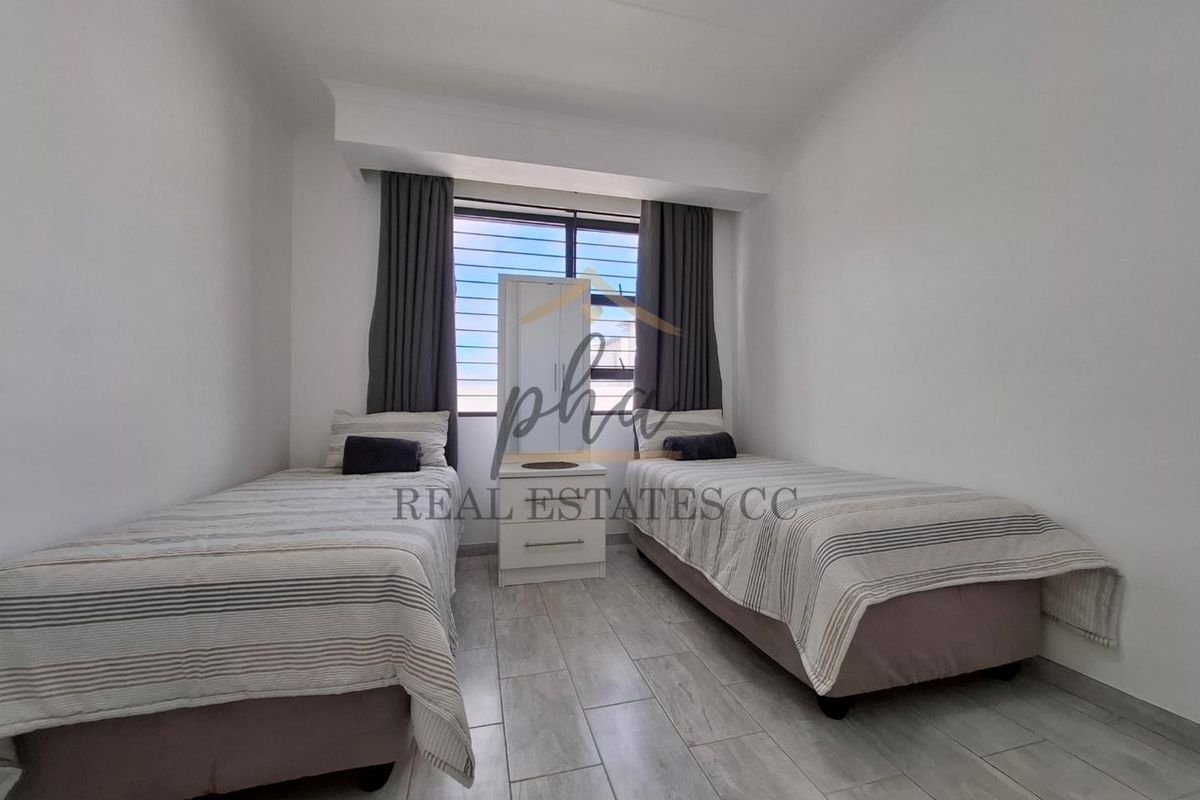 A well-maintained bedroom featuring neutral tiled flooring, large window with fitted curtains, and clean white walls.