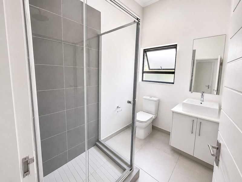 A modern, clean bathroom featuring a glass-enclosed shower with grey tiling, a white vanity with a basin, and a toilet.