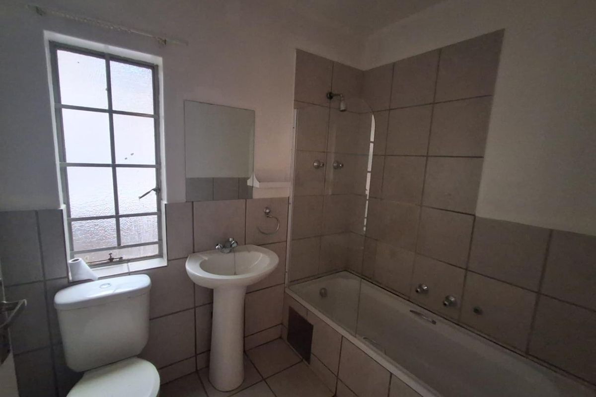 A functional bathroom featuring a pedestal basin, a toilet, and a bathtub with a shower mixer and glass screen.