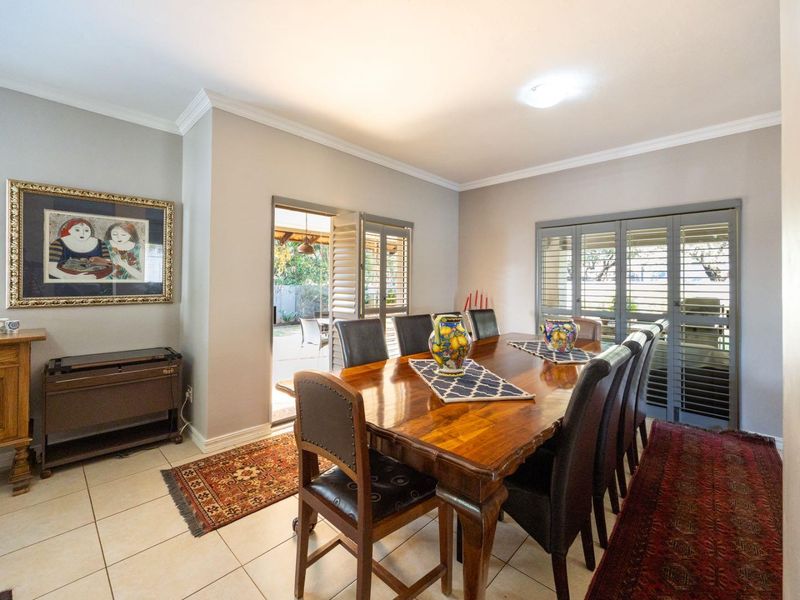 A well-maintained dining room featuring tiled flooring, crown molding, and plantation shutters with direct access to the outdoor patio area.