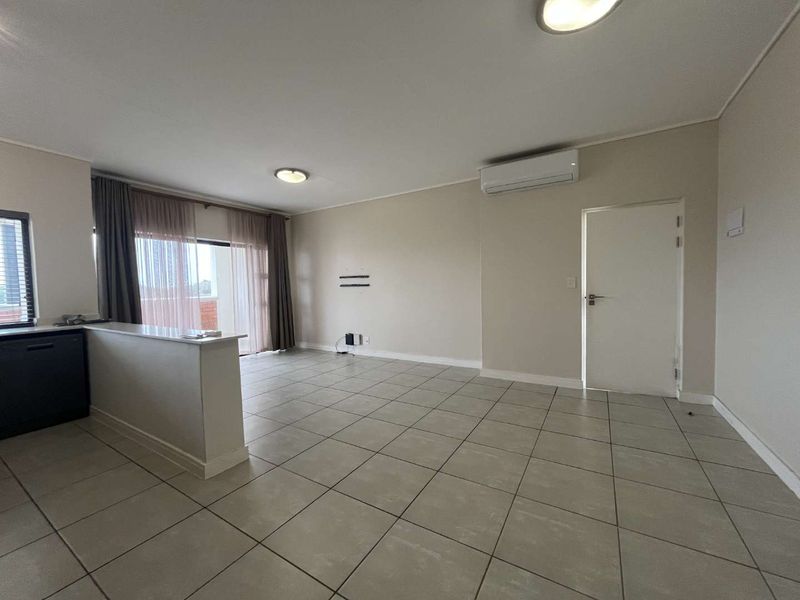 Spacious open-plan living area featuring neutral tiled flooring, a split-system air conditioner, and a breakfast bar, offering a bright and versatile layout.