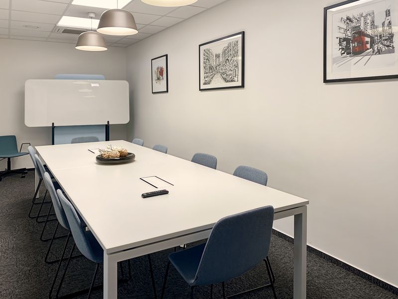 A modern, well-maintained office meeting room featuring a large conference table, suspended ceiling with recessed lighting, and professional carpeted flooring.