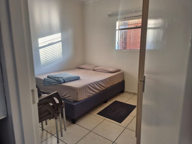 A functional bedroom featuring tiled flooring and a window with venetian blinds, offering a simple and practical living space.