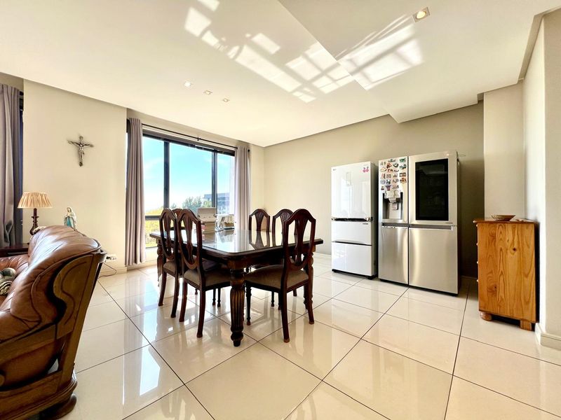 Spacious open-plan living and dining area featuring large format floor tiles, recessed ceiling lighting, and a large window providing ample natural light.