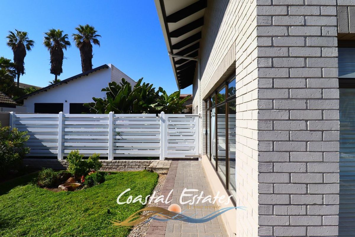 A side view of the property featuring a paved walkway, white horizontal slat fencing, and a well-maintained garden area.