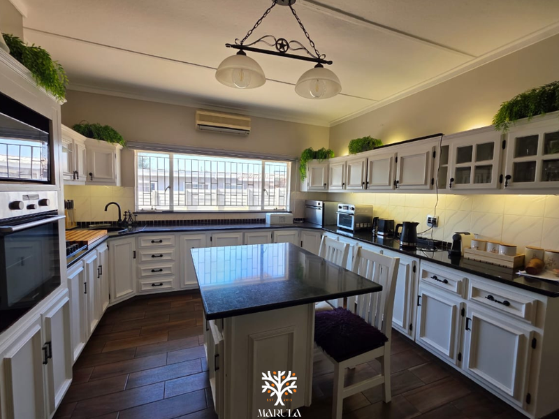 Spacious kitchen featuring white cabinetry, dark granite countertops, a central island, and integrated oven, complemented by warm under-cabinet lighting and tiled flooring.