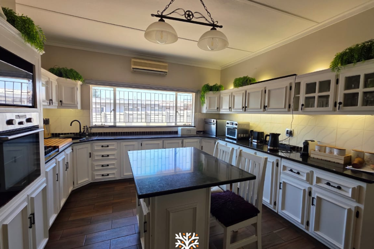 Spacious kitchen featuring white cabinetry, dark granite countertops, a central island, and integrated oven, complemented by warm under-cabinet lighting and tiled flooring.