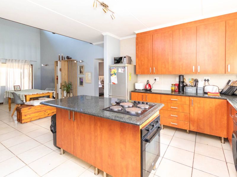 Open-plan kitchen featuring a central island with a built-in oven and hob, granite countertops, and ample wooden cabinetry, flowing into the dining area.