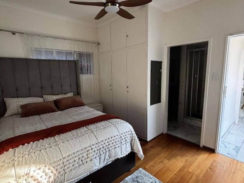 A well-maintained bedroom featuring laminate flooring, built-in cupboards, a ceiling fan, and direct access to an en-suite bathroom.
