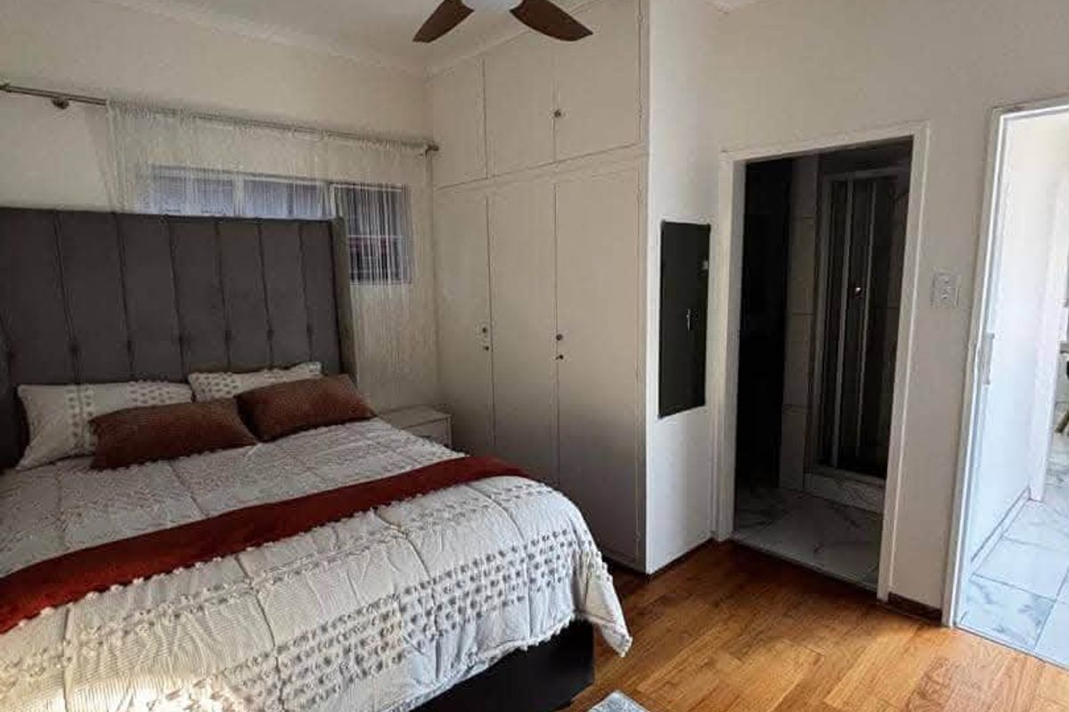 A well-maintained bedroom featuring laminate flooring, built-in cupboards, a ceiling fan, and direct access to an en-suite bathroom.