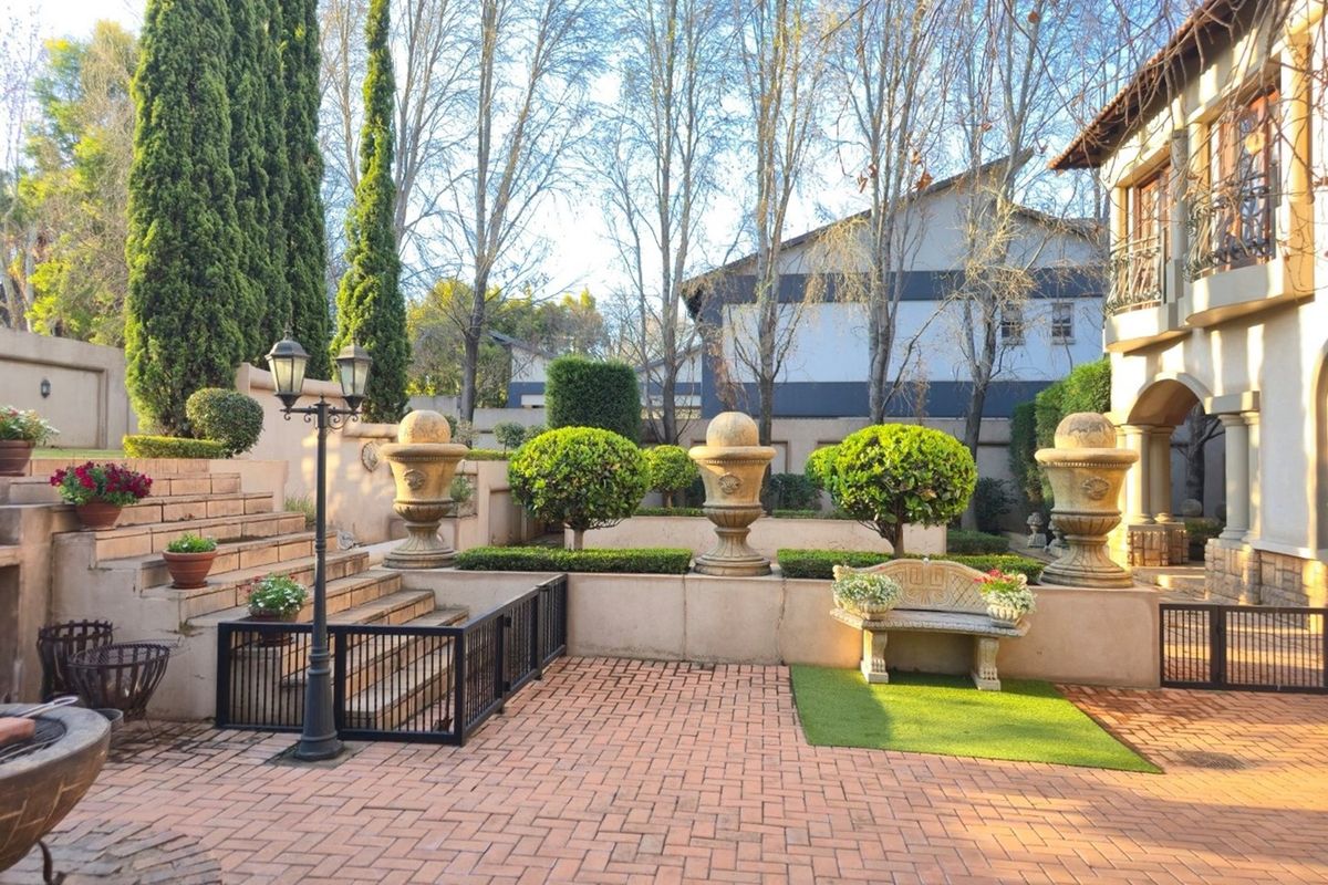 A well-maintained rear garden featuring brick paving, tiered retaining walls, decorative stone urns, and manicured hedges, providing an elegant outdoor entertainment space.
