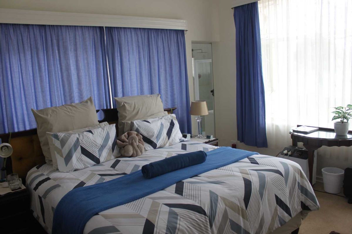 A bedroom featuring large windows with curtains and an en-suite bathroom visible in the background.