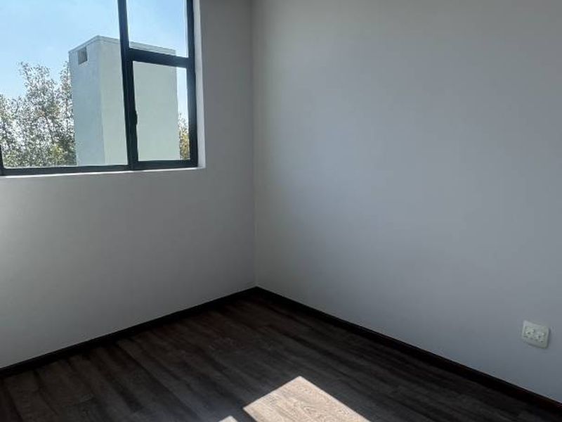 A bright, empty bedroom featuring modern laminate flooring, recessed downlights, and a large aluminium-framed window allowing for ample natural light.