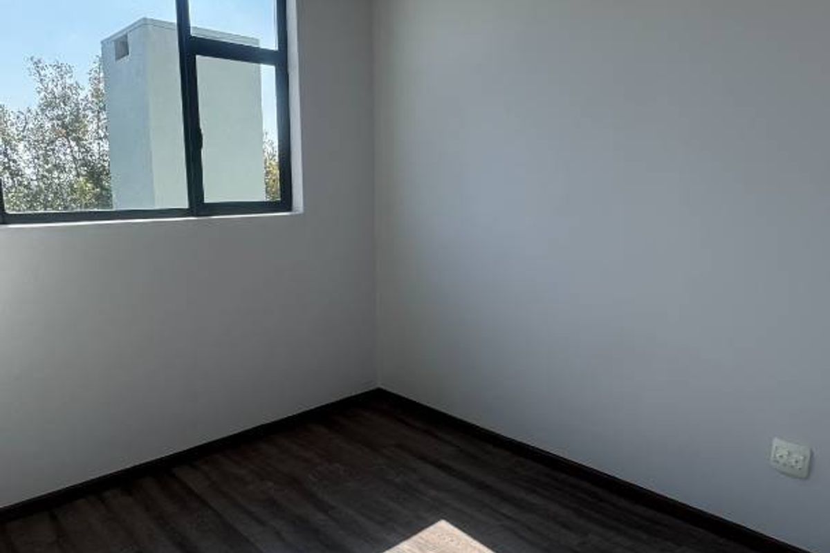 A bright, empty bedroom featuring modern laminate flooring, recessed downlights, and a large aluminium-framed window allowing for ample natural light.