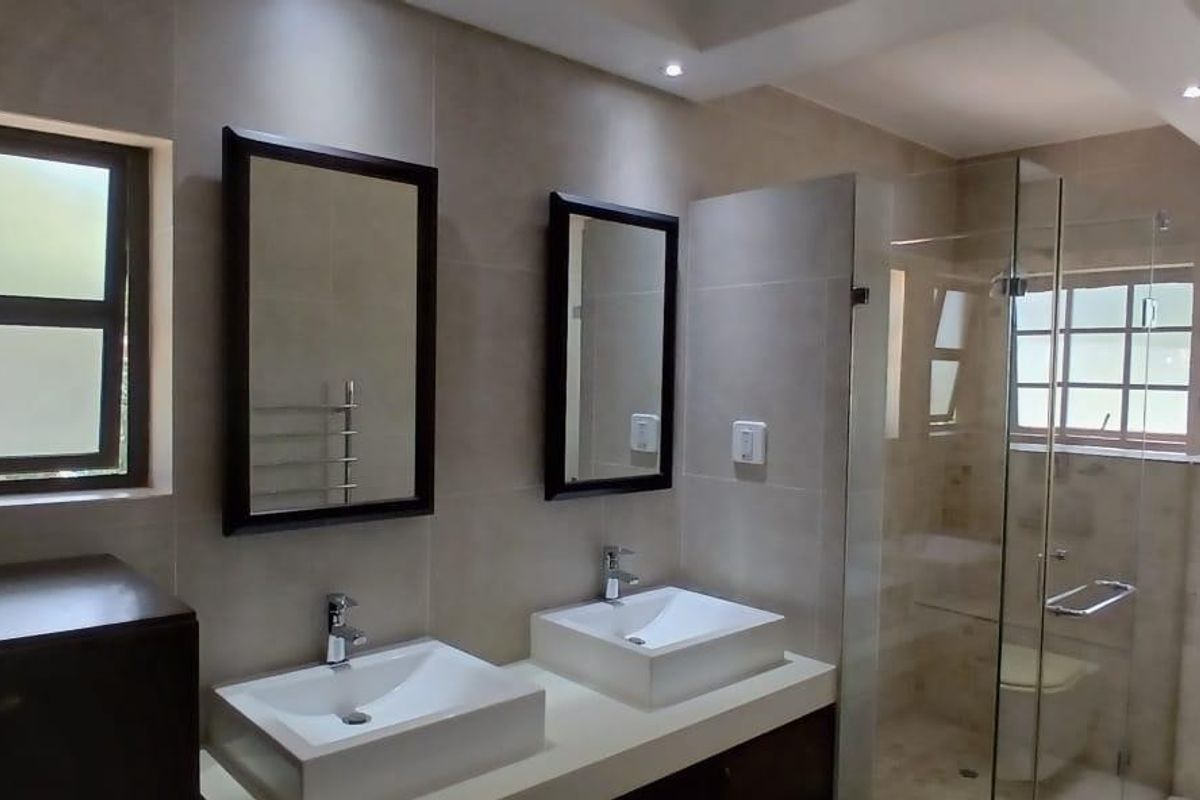Modern bathroom featuring a double vanity with vessel sinks, a glass-enclosed shower, wall-mounted toilet, and neutral floor-to-ceiling tiling.