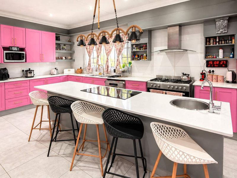 A vibrant, modern kitchen featuring bright pink cabinetry, a large central island with a gas cooktop, integrated appliances, and sleek quartz countertops.