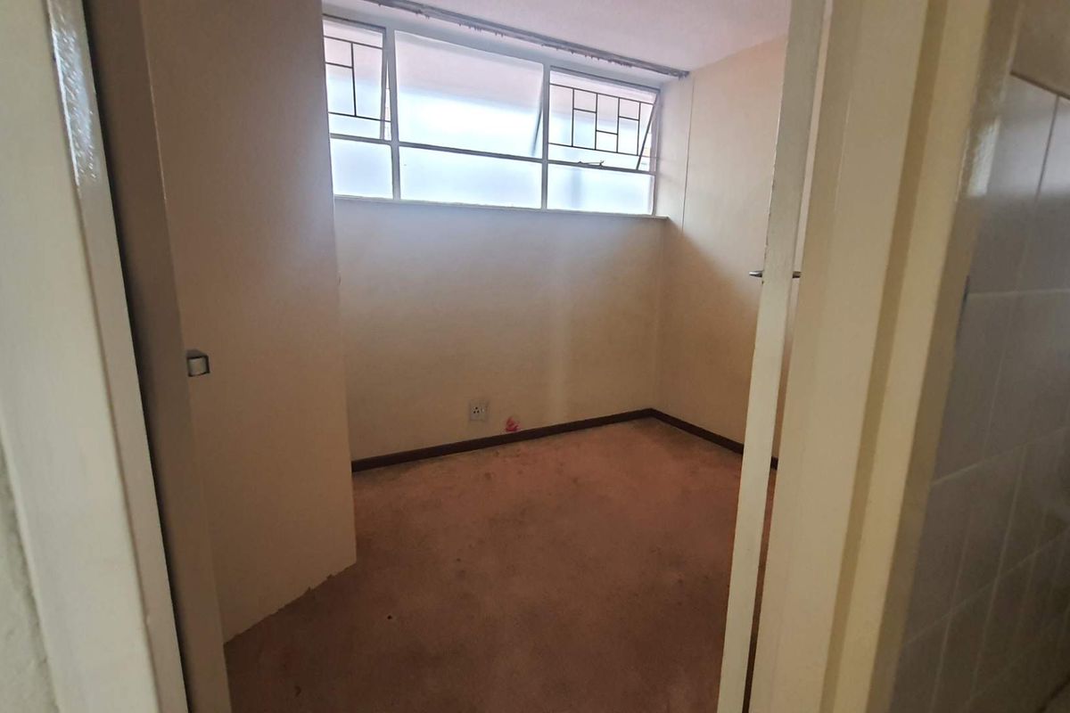 An empty bedroom featuring metal-framed windows and carpeted flooring, presenting a blank canvas ready for renovation and modernization.