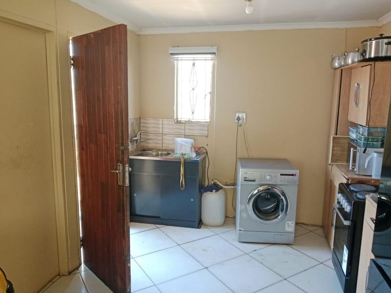 A functional laundry area featuring a stainless steel sink, tiled splashback, and built-in cabinetry with space for a washing machine.