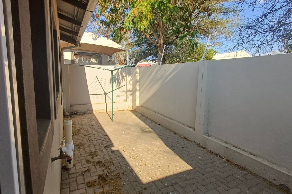A private paved rear courtyard featuring perimeter walls with electric fencing and an external water tap.