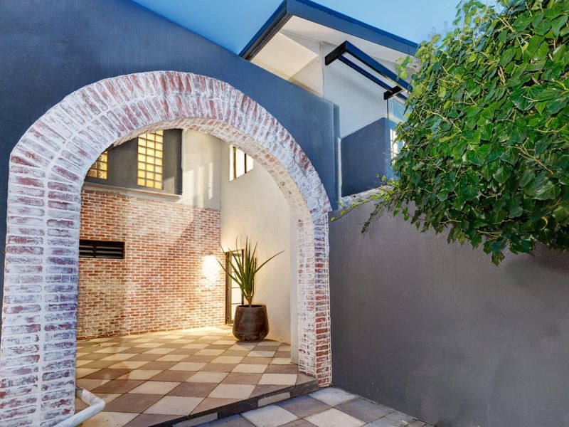 A charming covered patio area featuring a distinctive brick archway, tiled flooring, and exposed brick accents, creating a unique architectural entrance or outdoor space.