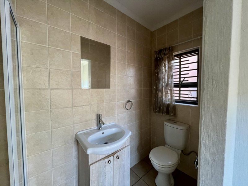 A functional bathroom featuring a vanity cabinet with basin, toilet, and a shower enclosure, finished with neutral wall and floor tiling.