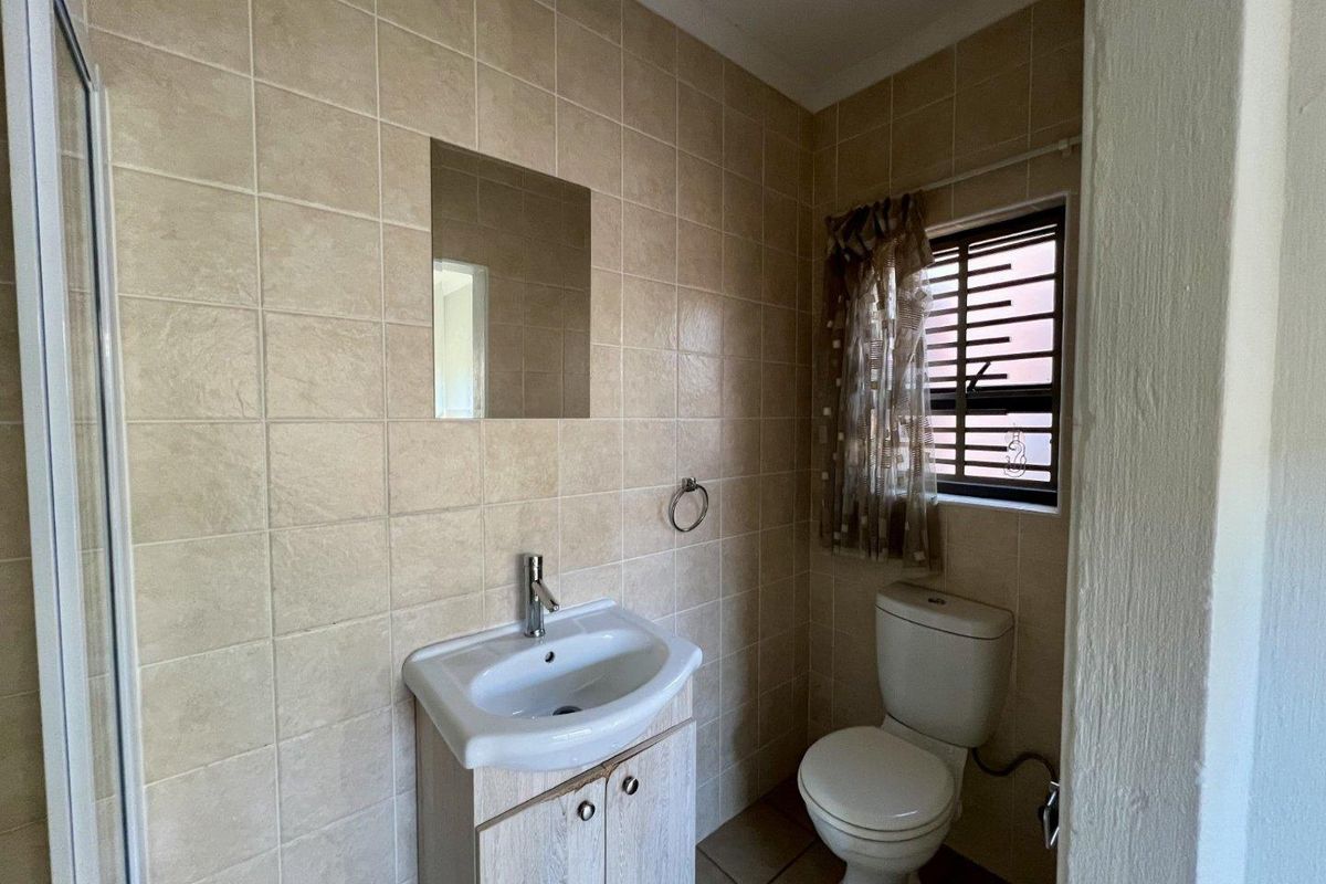 A functional bathroom featuring a vanity cabinet with basin, toilet, and a shower enclosure, finished with neutral wall and floor tiling.