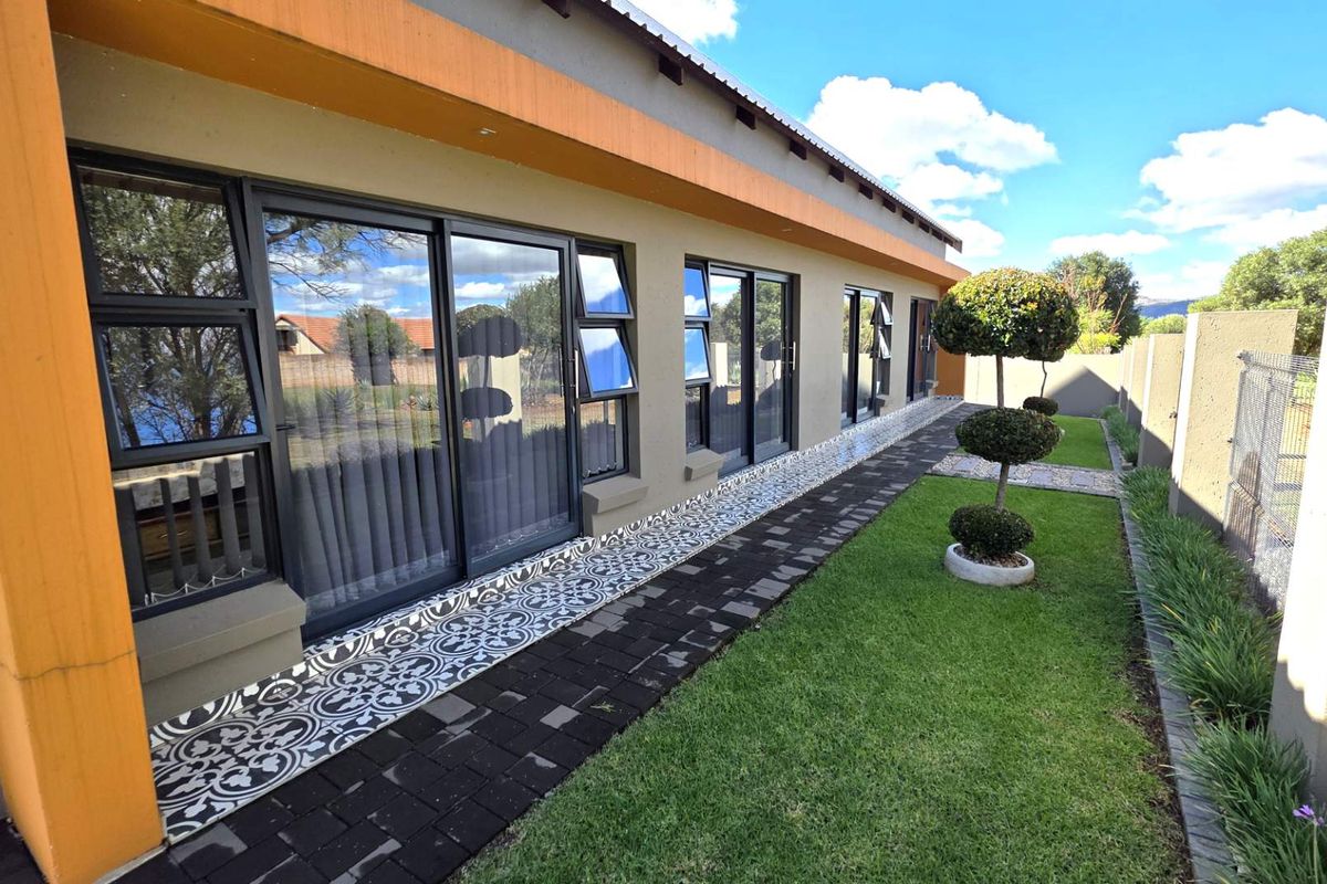 A well-maintained rear exterior view featuring a paved walkway, manicured lawn, and large sliding glass doors providing seamless indoor-outdoor access.