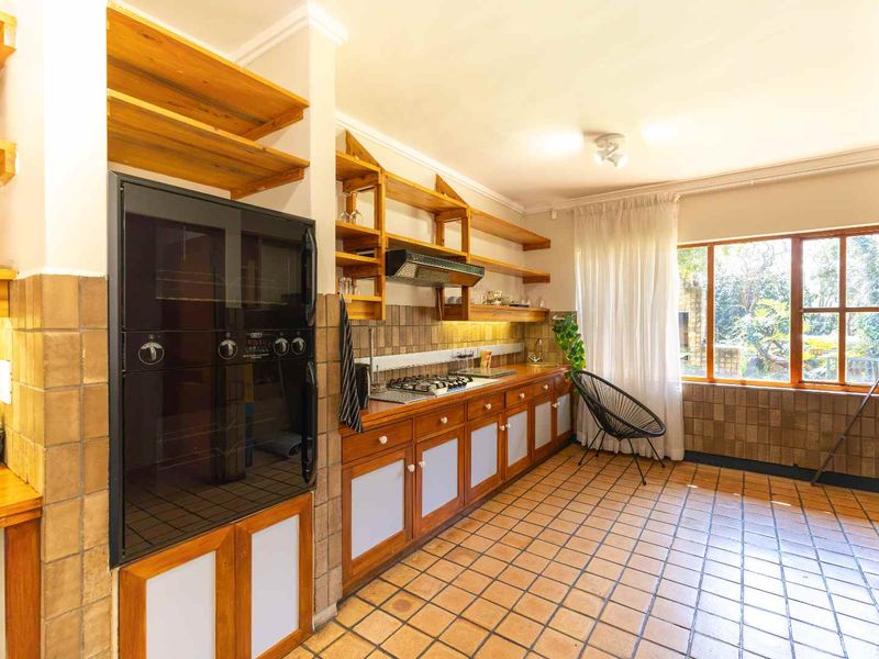A functional kitchen featuring wooden cabinetry, built-in oven, gas hob, and tiled flooring, offering a classic layout with ample storage and natural light.