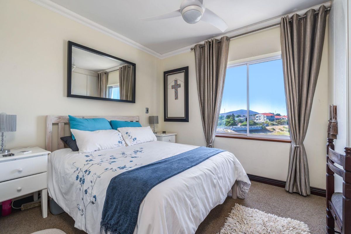A well-lit bedroom featuring a ceiling fan, carpeted flooring, and a window offering scenic views of the surrounding area.