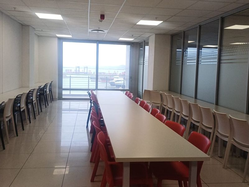 A spacious office area featuring tiled flooring, suspended ceilings with recessed lighting, and glass partitions, offering a functional workspace with natural light.