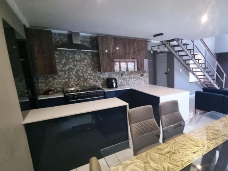 Modern open-plan kitchen featuring dark cabinetry, stone countertops, gas stove, and an integrated staircase leading to the upper level.