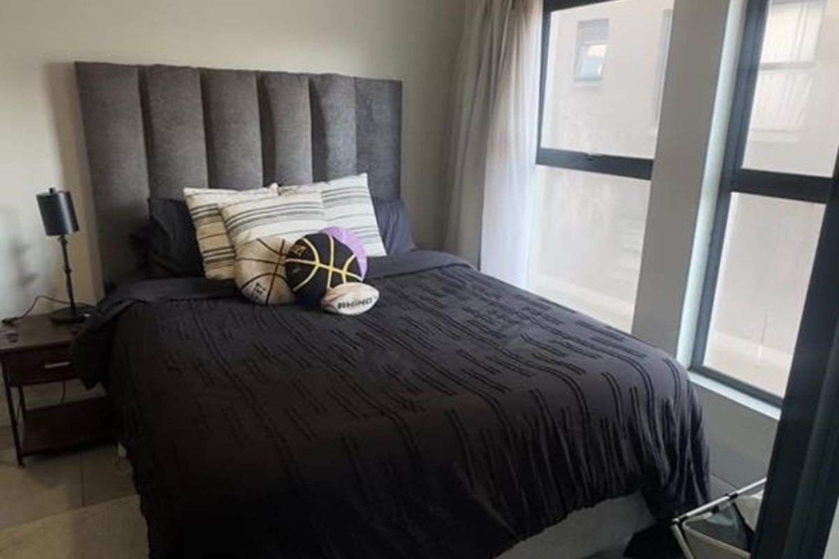 A well-lit bedroom featuring neutral tiled flooring, modern pendant lighting, and large aluminium-framed windows allowing for natural light.
