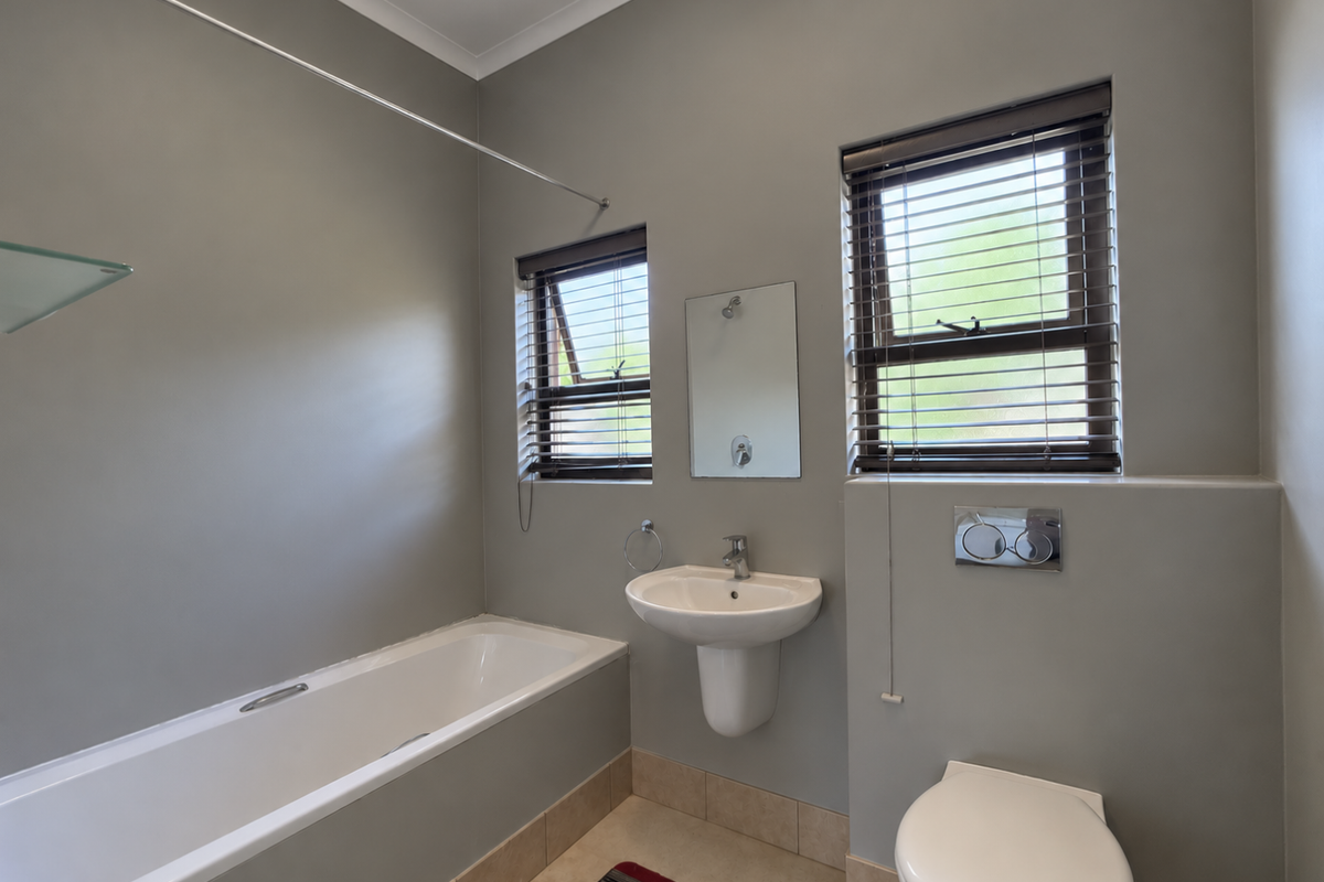 A clean, functional bathroom featuring a pedestal basin, wall-mounted toilet with concealed cistern, and a bathtub with a shower curtain rod.