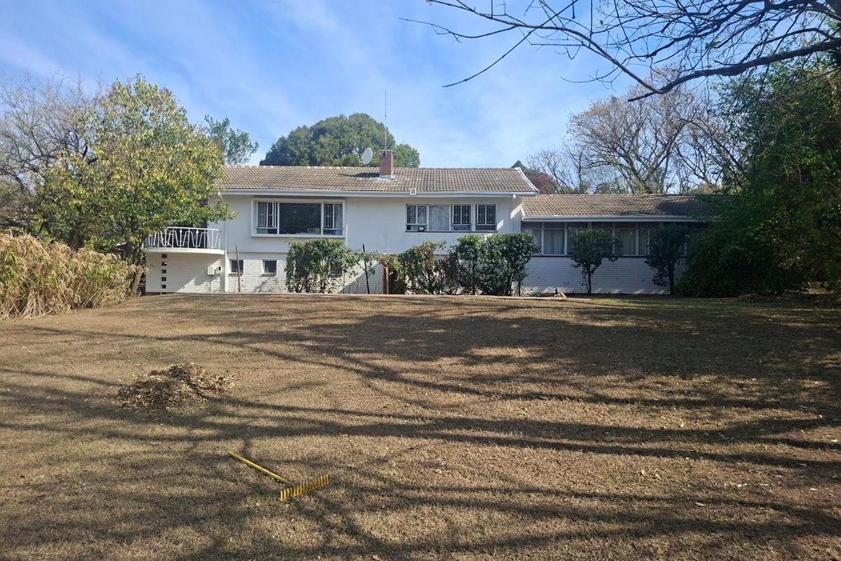 A rear view of a single-story residential house featuring a tiled roof, white brick exterior, and a spacious backyard garden.