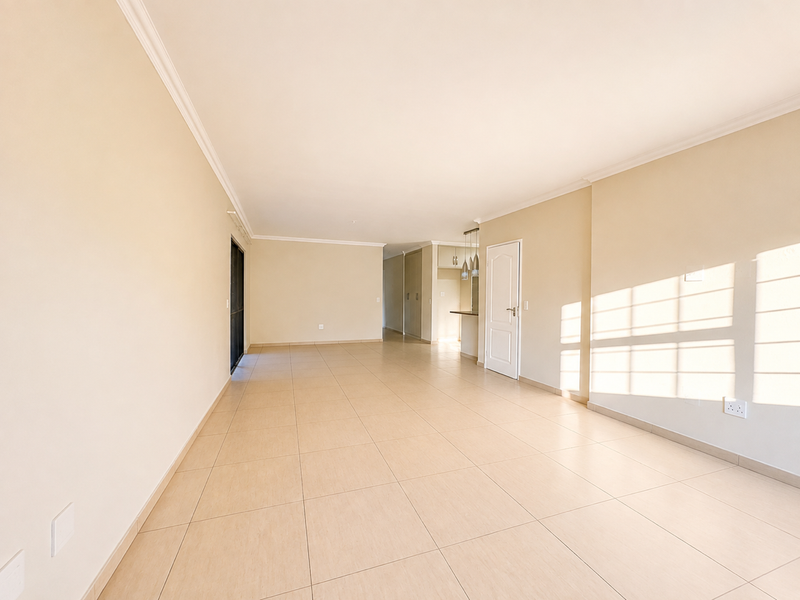 Spacious open-plan living area featuring neutral tiled flooring, cove cornicing, and a functional kitchen area with a breakfast counter.