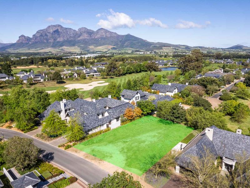 An aerial view of a vacant residential plot situated within a scenic golf estate, featuring mountain views and established surrounding homes.