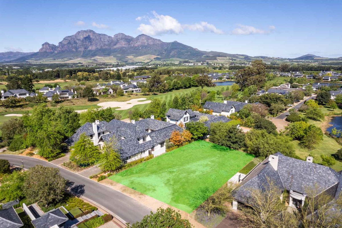 An aerial view of a vacant residential plot situated within a scenic golf estate, featuring mountain views and established surrounding homes.
