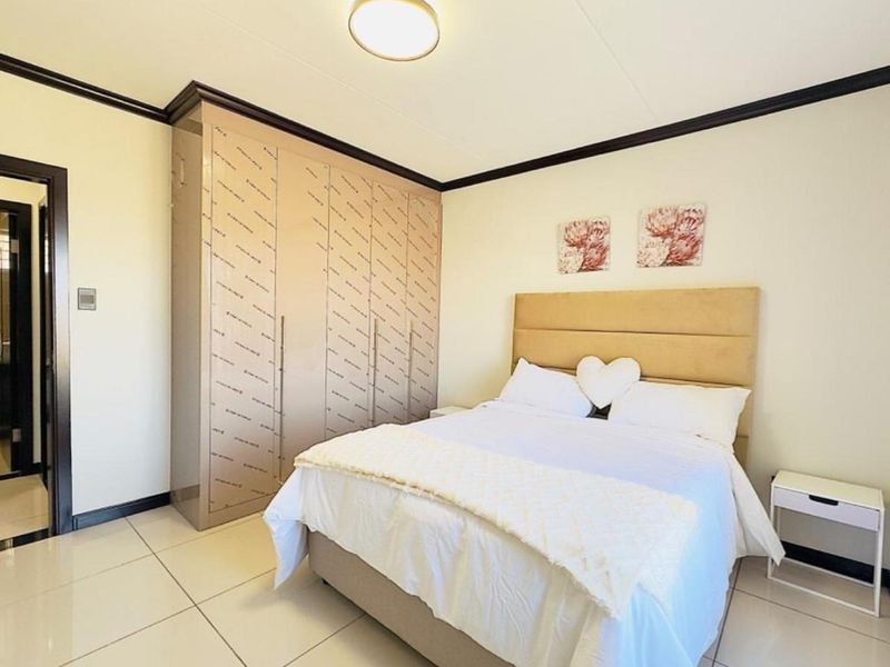 A well-maintained bedroom featuring large built-in cupboards with protective film still attached, neutral tiled flooring, and a modern ceiling light fixture.
