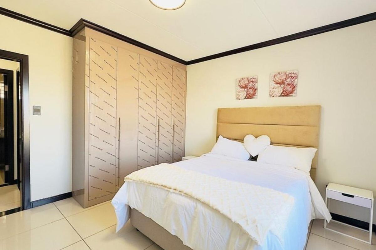 A well-maintained bedroom featuring large built-in cupboards with protective film still attached, neutral tiled flooring, and a modern ceiling light fixture.