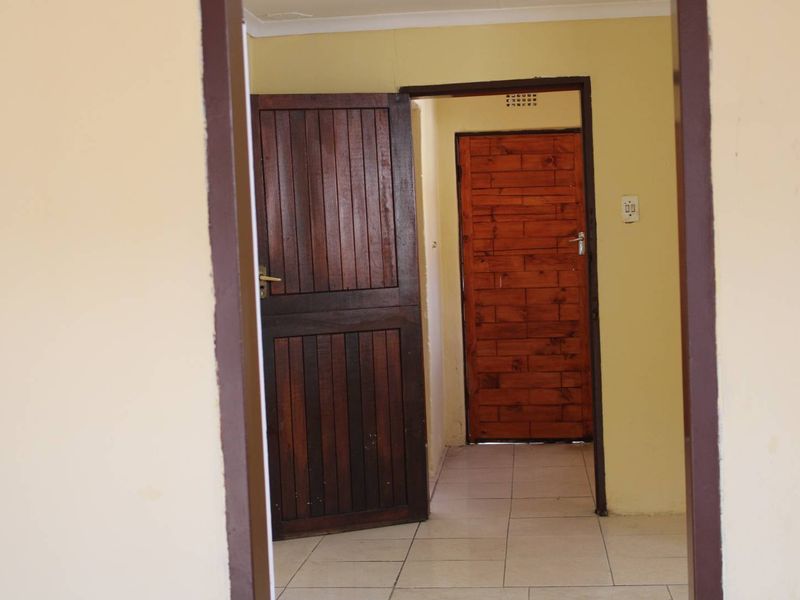 A simple interior hallway featuring tiled flooring and wooden doors, providing access between rooms in the property.