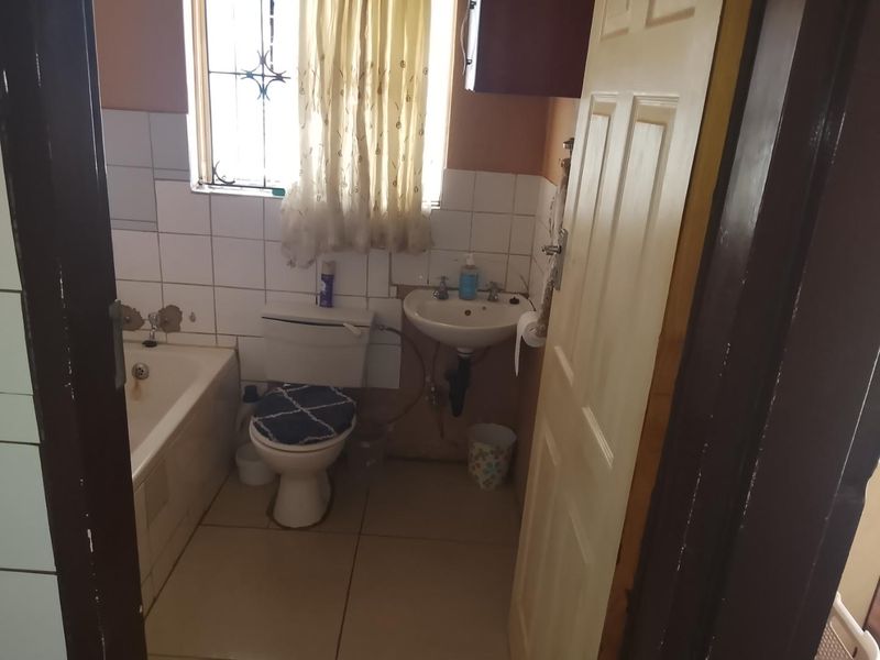 A functional bathroom featuring a bathtub, pedestal basin, and toilet, with tiled finishes and security bars on the window.