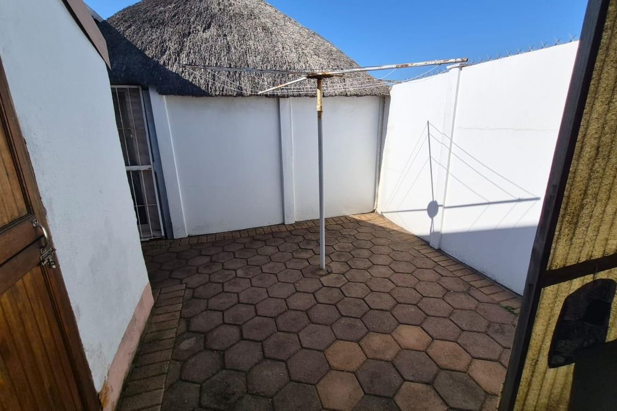 A private rear courtyard area featuring paved flooring, a rotary clothesline, and enclosed by boundary walls, with a view of a thatched roof structure.