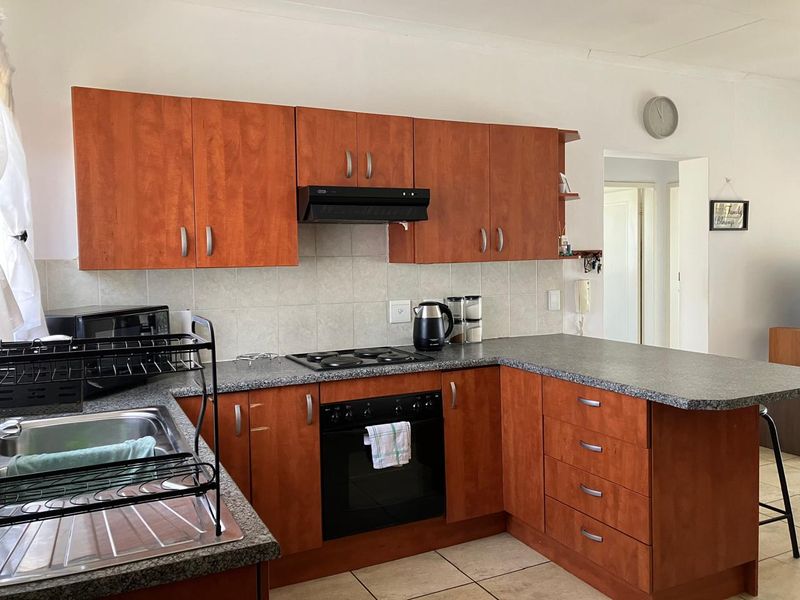 Functional kitchen featuring wood-look cabinetry, granite-style laminate countertops, built-in oven, electric hob, extractor fan, and tiled flooring.