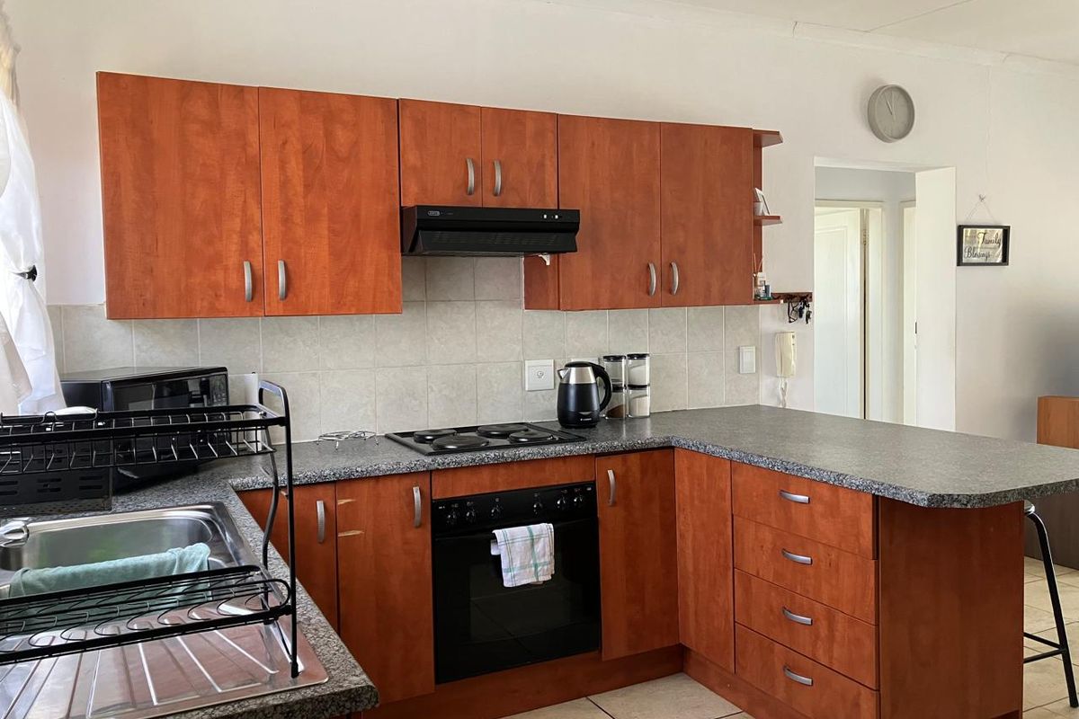 Functional kitchen featuring wood-look cabinetry, granite-style laminate countertops, built-in oven, electric hob, extractor fan, and tiled flooring.