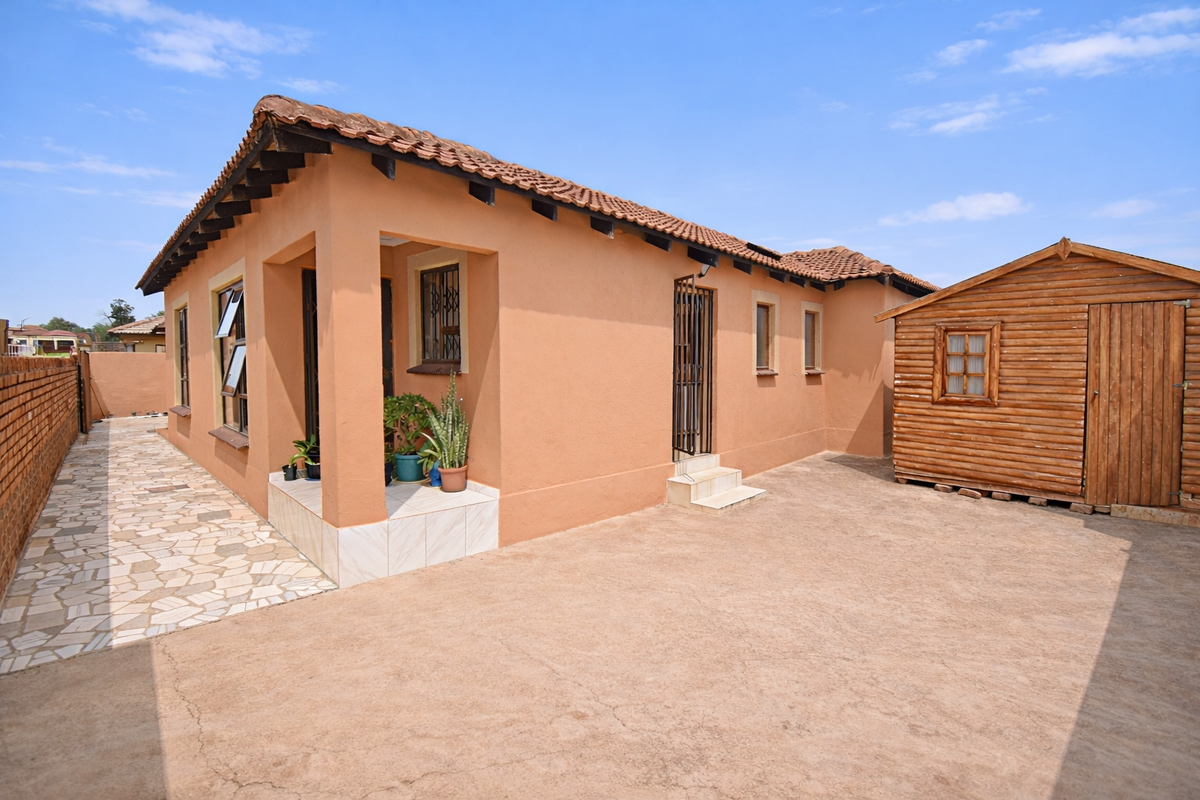 Rear view of the property featuring a terracotta tiled roof, paved walkway, and a detached wooden garden shed within a walled yard.