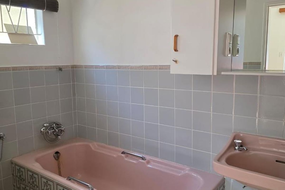 A dated bathroom featuring a vintage pink bathtub and matching wall-mounted basin, complemented by patterned tile accents and a wall-mounted storage cabinet.